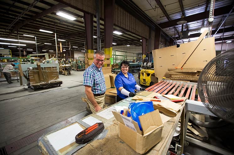 Two workers smiling and looking at boxes and plans in the factory