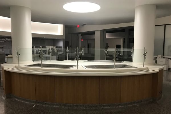 Empty food station in open cafeteria with sneeze guards lining each food station