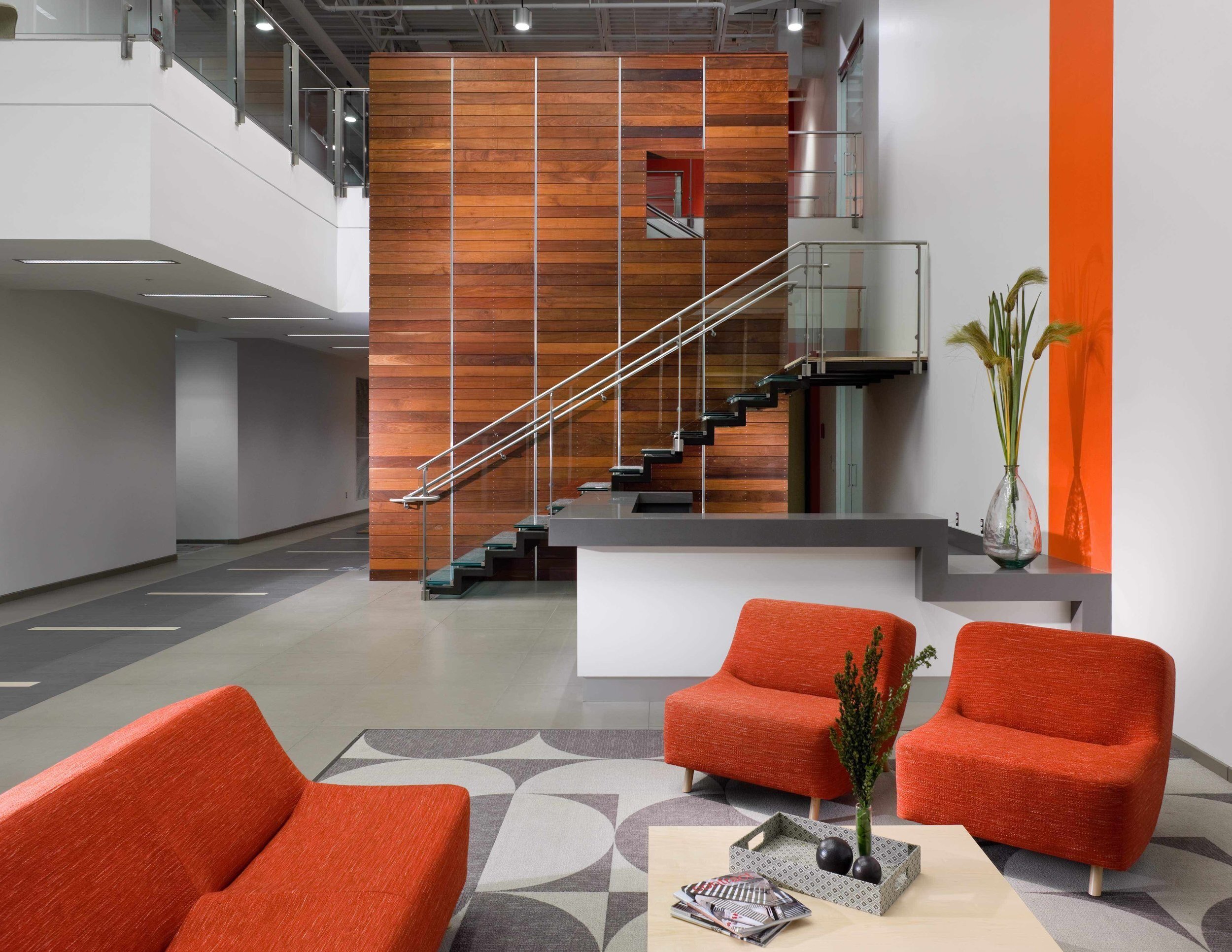 Modern office with nice wood wall behind staircase with glass walls and orange accent furniture