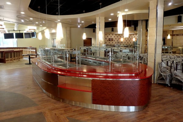 Red food service station in center of cafeteria with sneeze guard surrounding station